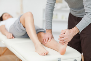 Picture of a Physical Therapist (male) with one hand on a woman's knee and the other hand on her foot. She is lying on her back