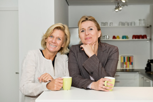 Picture of two females standing up against a counter next to each other holding a cup of coffee