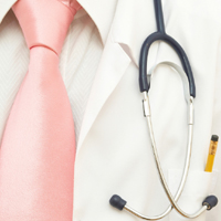 Picture of a Physicians tie, medical coat, pen in pocket, and stethoscope hanging down in front of his pocket on his chest.